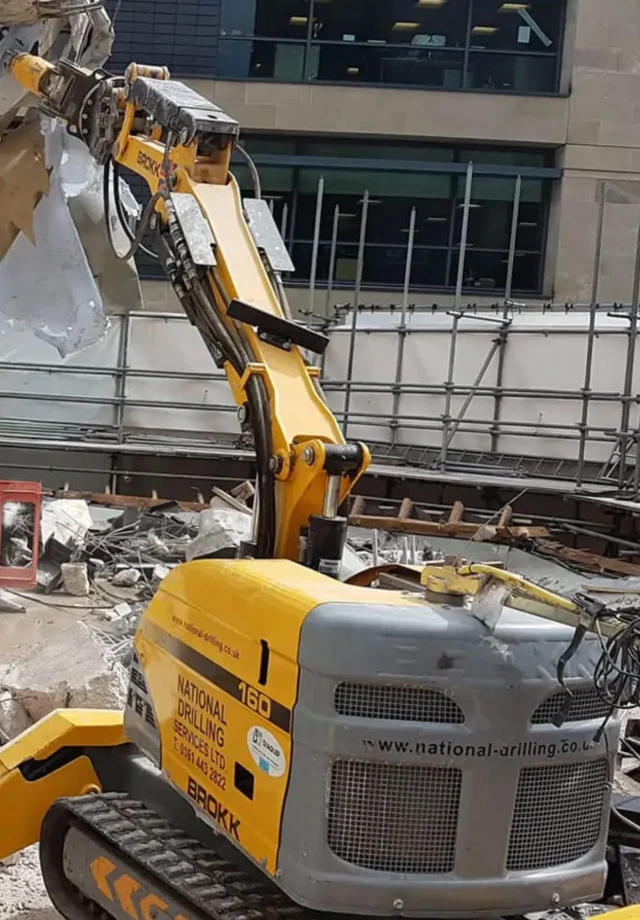 Brokk robotic demolition machine operated by National Drilling Services in construction site, showcasing advanced demolition technology and safety standards.